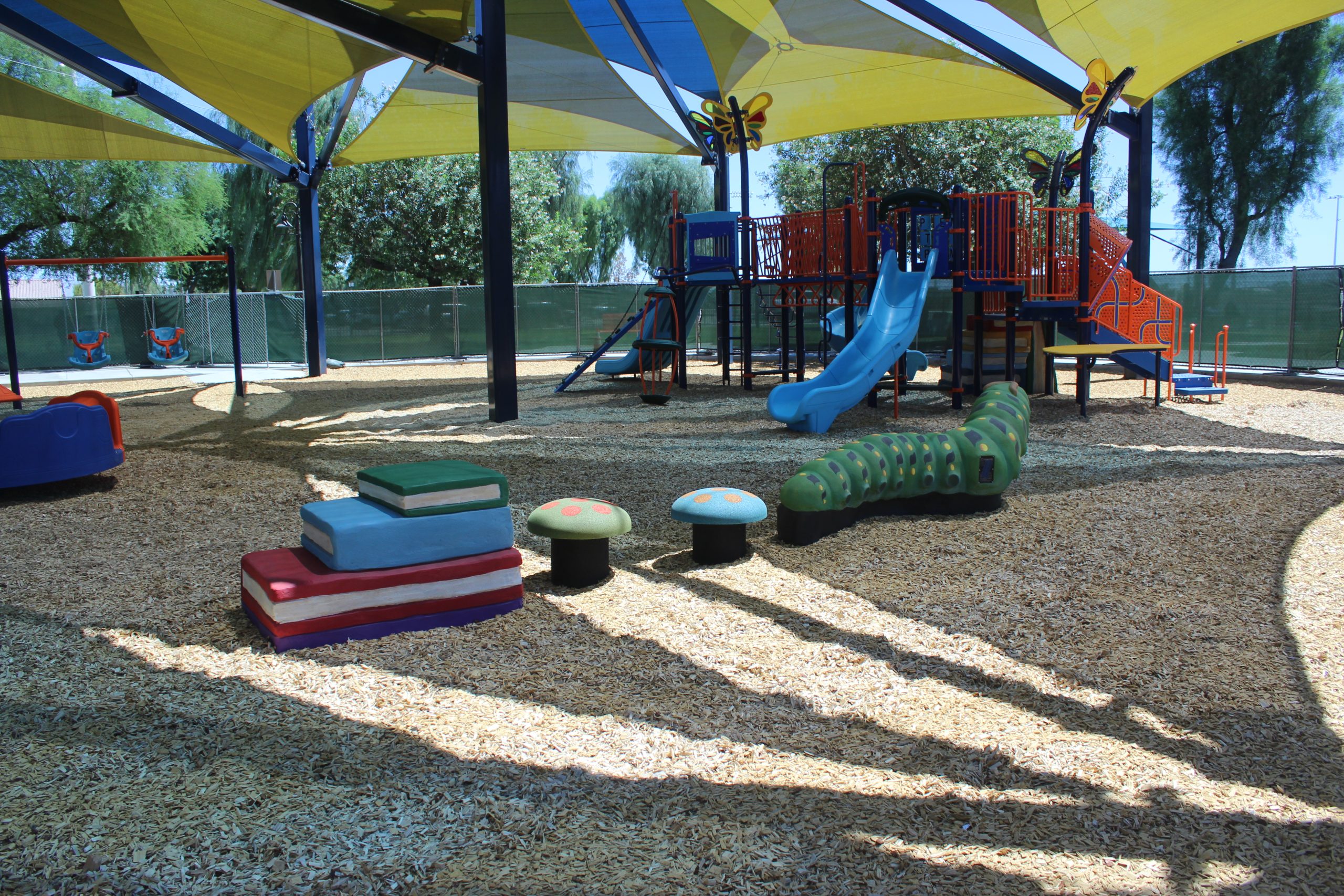 Photo highlighting the vibrant and imaginative playground design at the City of La Quinta, featuring a colorful caterpillar climber, butterfly elements, and book-themed structures that bring the space to life.